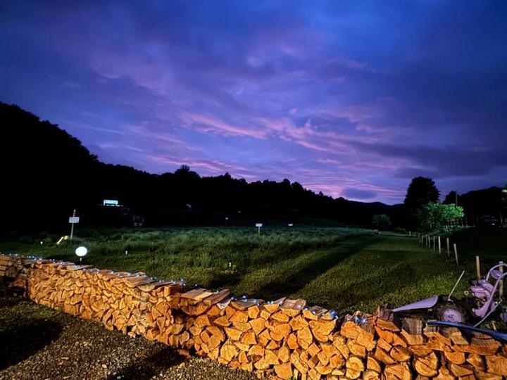 The stacked-wood wall lit at dusk under a purple sky